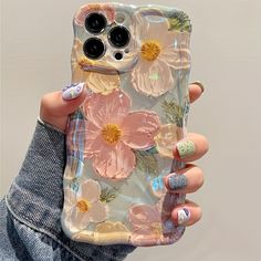 a woman holding up her phone case with flowers on the front and sides, while wearing jeans