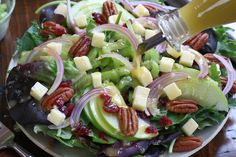 a salad with apples, cheese and pecans is being drizzled with dressing