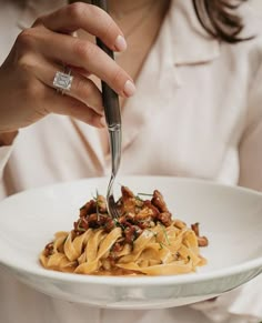 a woman is holding a plate of pasta with meat and vegetables on it while she holds a fork in her hand