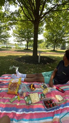 a person sitting on a blanket with food in front of them at a picnic table