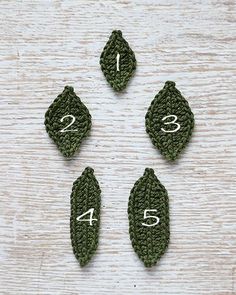 four crocheted leaves arranged in the shape of numbers on a white wooden surface