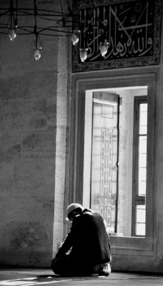 a man sitting on the floor in front of a window with arabic writing on it