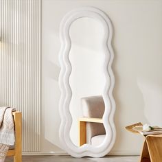 a large white mirror sitting on top of a wall next to a chair and table