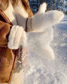 a woman is throwing snow in the air with her mittens on and one hand