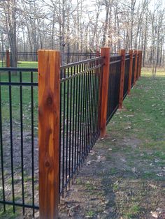 a black fence with wooden posts in the grass