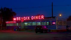 a diner that is lit up at night with neon signs on the side of it