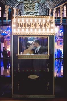 a man and woman are standing in front of a ticket booth with lights on it