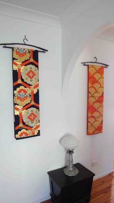 two wall hangings on the side of a white wall next to a black table