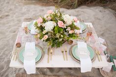 the table is set with flowers and place settings for dinner on the beach sand dunes