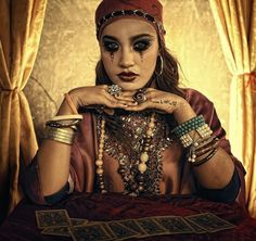 a woman with makeup and jewelry on her face sitting in front of a table full of cards