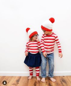 two young children wearing matching red and white striped shirts, blue skirts, and knitted hats