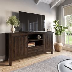 a large flat screen tv sitting on top of a wooden entertainment center next to a window