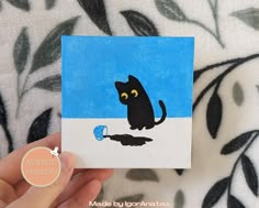 a hand is holding up a small card with a black cat painted on the front