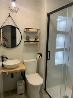 a white toilet sitting next to a walk in shower under a round mirror on a wall