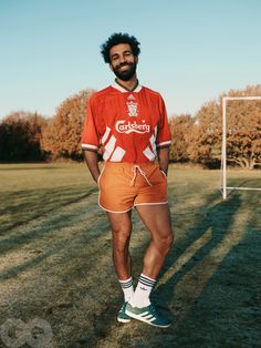 a man standing in front of a soccer goal wearing an orange shorts and white shirt