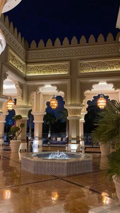 the inside of a building with columns and lights on it at night in front of a fountain