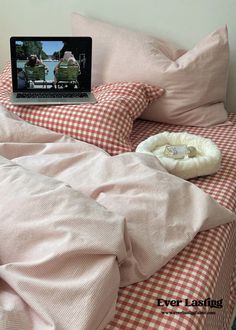 an open laptop computer sitting on top of a bed covered in pink sheets and pillows