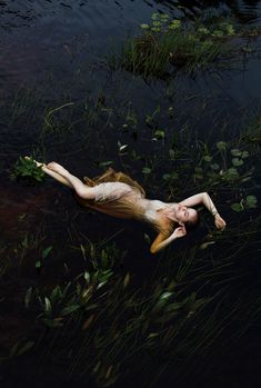 a woman floating in the water surrounded by plants