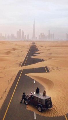 two people sitting on top of a car in the middle of an empty desert road