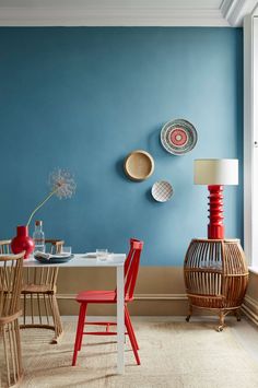 a dining room with blue walls and red chairs in front of a white table surrounded by plates on the wall