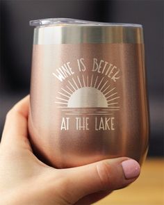 someone holding up a wine glass with the words wine is better at the lake