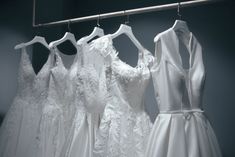 four white dresses are hanging on a rack