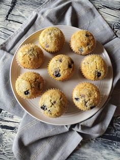 a white plate topped with muffins sitting on top of a wooden table next to a gray napkin