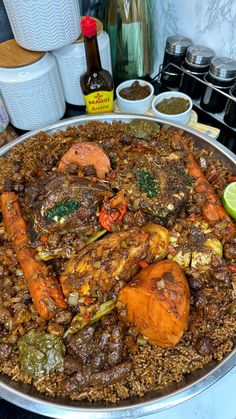 a large metal pan filled with food on top of a counter next to spices and condiments