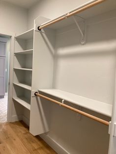 an empty room with white shelves and wood flooring on the side walk in closet