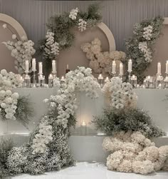 an arrangement of flowers and candles in front of a wall with floral arrangements on it