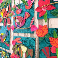 colorful paper fish are hanging on the side of a wooden wall with flowers and leaves