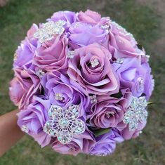 a bridal bouquet with purple roses and crystal brooches is held in someone's hand