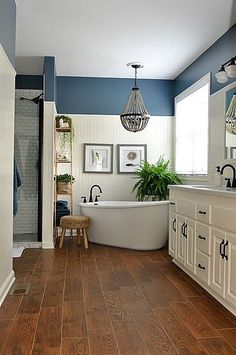 a bathroom with blue walls and wood flooring is pictured in this image, there is a bathtub on the far side of the room