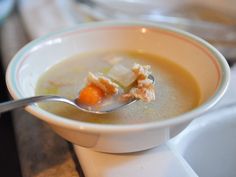 a white bowl filled with soup on top of a counter next to a silver spoon