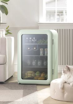 a white cat sitting on top of a ottoman next to a mini fridge