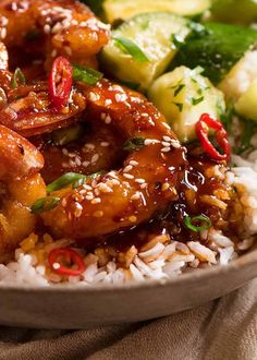 a white plate topped with rice and shrimp next to cucumber, broccoli and cucumbers