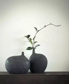 two gray vases sitting on top of a table with a plant in one pot