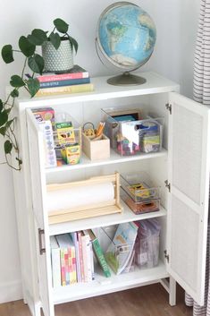 a white bookcase with books and toys on top of it next to a potted plant