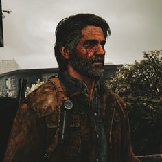 a man with a beard and leather jacket standing in front of a building on a cloudy day