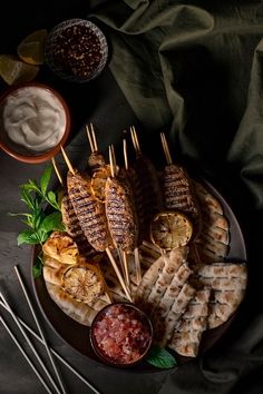 grilled chicken and waffles with dipping sauce on a black plate, surrounded by other appetizers