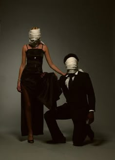 a woman in a black dress standing next to a man wearing a mask