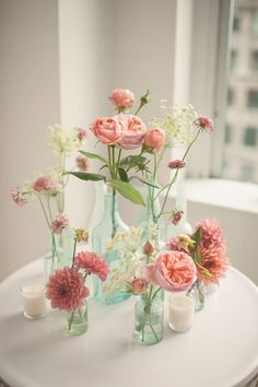 several vases with flowers and candles are on a table in front of a window