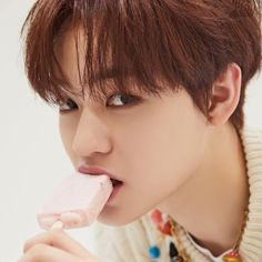 a young man with brown hair is eating a piece of pink ice cream on his tongue