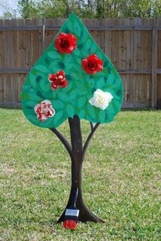 a paper plate christmas tree with red and white flowers on it in the grass near a fence