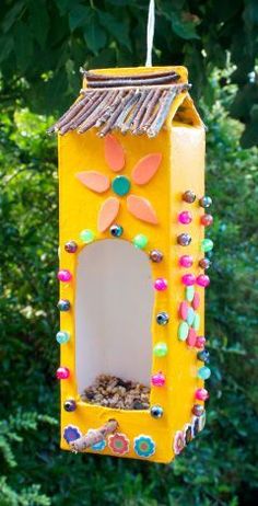 a yellow bird feeder hanging from a tree with lots of beads on it's side