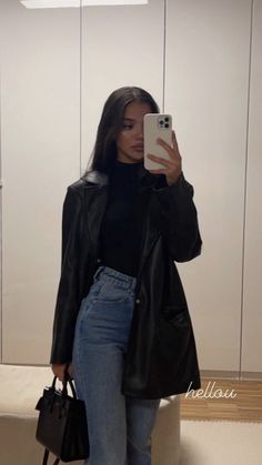 a woman taking a selfie in front of a mirror wearing jeans and a leather jacket