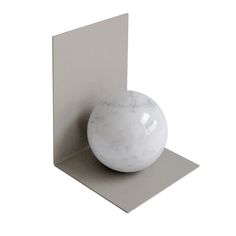 a white marble ball sitting on top of a metal shelf next to a square piece of paper