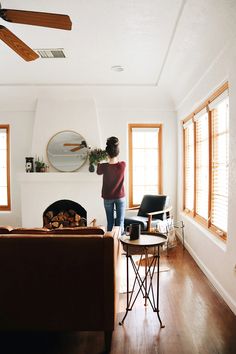 a woman standing in the middle of a living room with a fireplace and ceiling fan