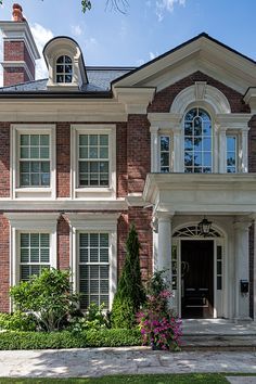 a large brick house with white trim and arched windows on the front door, surrounded by lush greenery