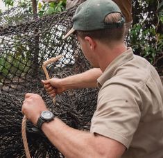 a man holding onto a rope while standing next to an animal in a netted enclosure